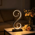 Lámpara de Mesa LED Espiral en S Negra USB encendida sobre un escritorio de madera