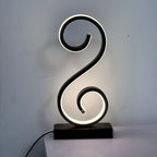 Lámpara de Mesa LED Espiral en S Negra USB con luz fría encendida en un estudio